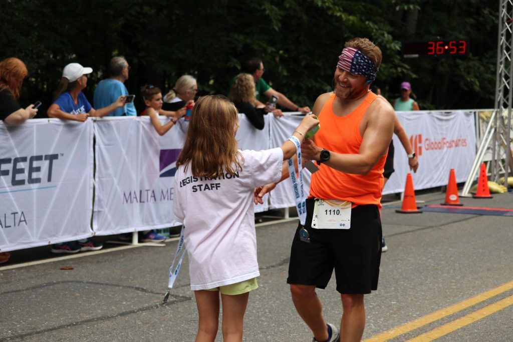 Volunteer Race Registrar also helps with handing out medals to the race finishers.